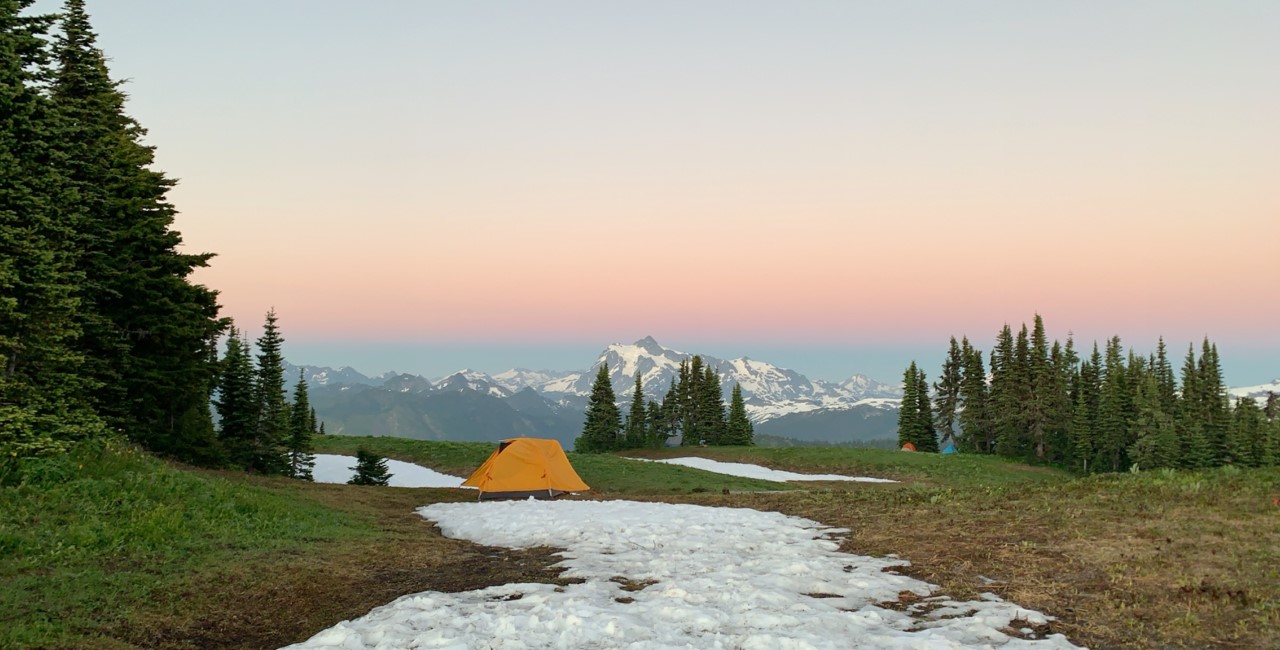 a yellow tent next to snow with a sunset in the background